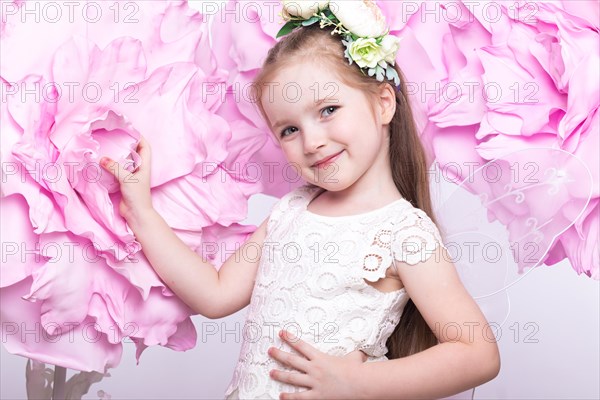 Little fairy girl in white dress on a background of flowers. Photo taken in studio