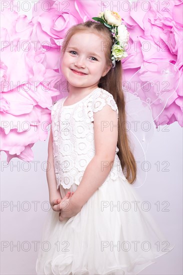 Little fairy girl in white dress on a background of flowers. Photo taken in studio