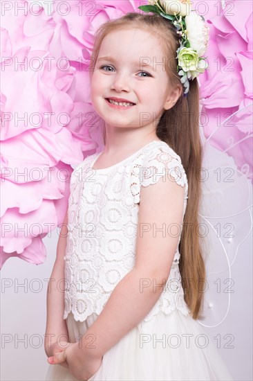 Little fairy girl in white dress on a background of flowers. Photo taken in studio