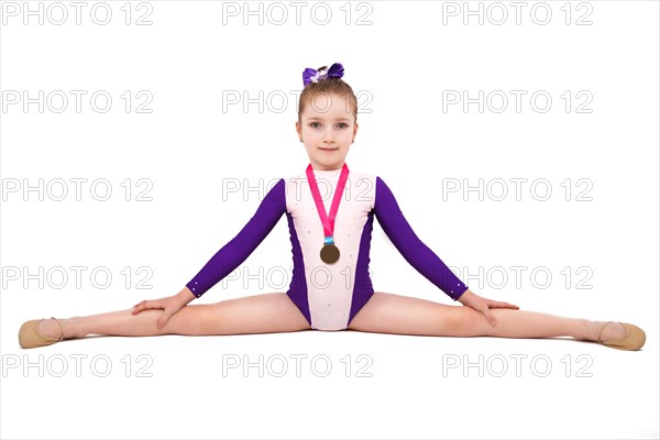 Little girl gymnast with a medal in a sports swimsuit doing exercises. Photo taken in the studio on a white background