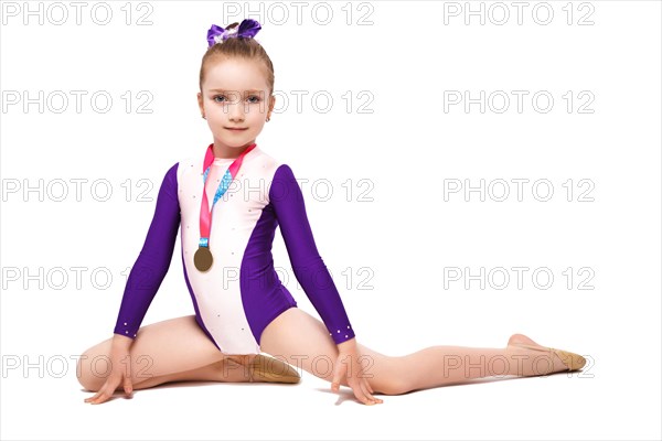 Little girl gymnast with a medal in a sports swimsuit doing exercises. Photo taken in the studio on a white background