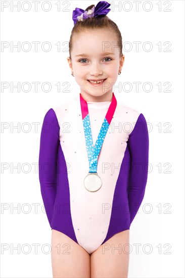 Little girl gymnast with a medal in a sports swimsuit doing exercises. Photo taken in the studio on a white background