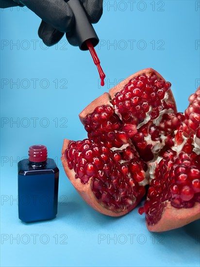 Bright bottle of nail polish on a blue background with pomegranate fruits. Manicure design