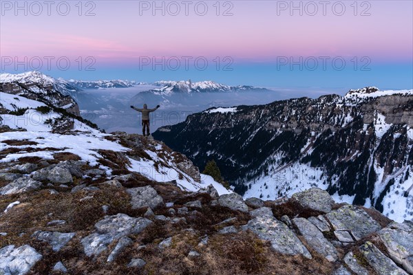 Man looking into the valley in front of sunrise with the colours of the earth's shadow on the horizon