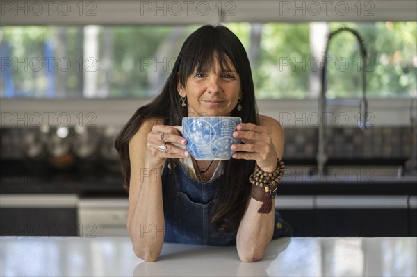 Portrait of a smiling woman enjoying a relaxing coffee break at home while looking at camera