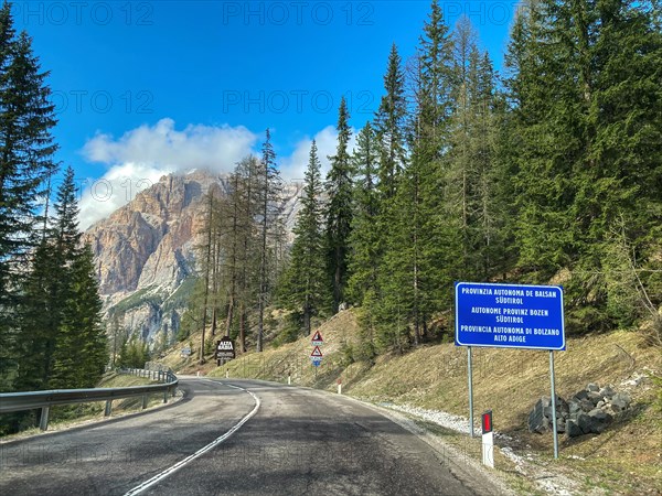 Mountain road behind Passo di Valparola with view of sign marking border between Veneto and Province of Bolzano South Tyrol