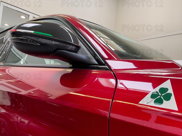 Detail of rear view mirror with carbon optic fairing with coloured stripes of Italian national colour flag Tricolore historical modern signet logo marking of Alfa Romeo Quadrifoglio green four-leaf clover on white triangle for sporty cars race car on limited to 500 pieces Italian sports car Alfa Romeo Giulia GTAm