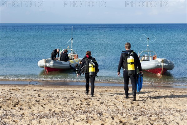 Divers Sport divers running with scuba equipment compressed air tanks across beach sandy beach from Mediterranean Sea to inflatable boat