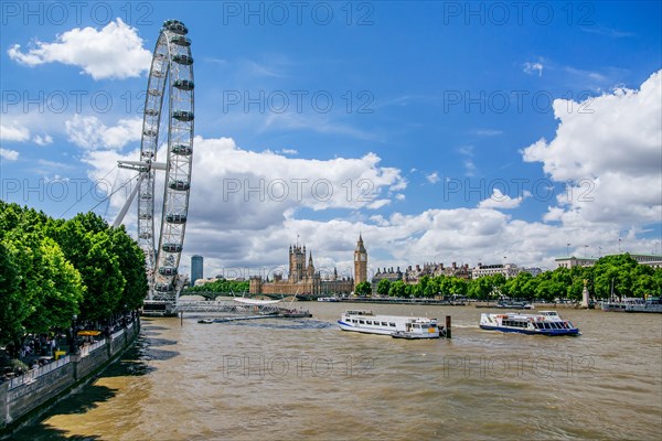 London Eye Ferris Wheel on the banks of the Thames with excursion boats and the Houses of Parliament