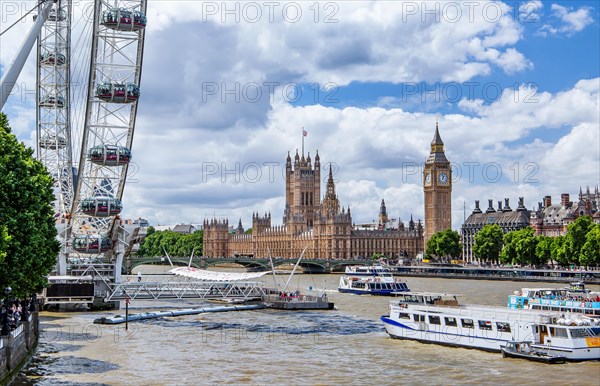 London Eye Ferris Wheel on the banks of the Thames with excursion boats and the Houses of Parliament