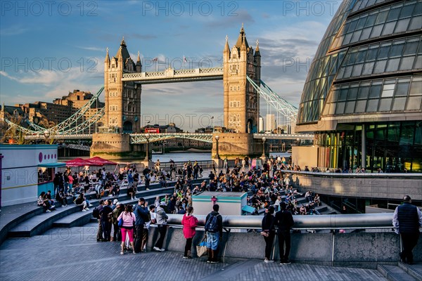 Spectators at The Scoop amphitheatre with London City Hall and Tower Bridge over the Thames in the evening sun