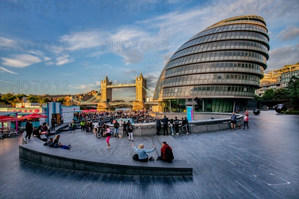 Spectators at The Scoop amphitheatre with London City Hall and Tower Bridge over the Thames in the evening sun