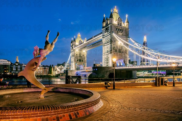 Sculpture Girl with Dolphin in front of Tower Bridge over the Thames at dusk