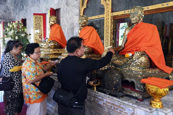 Believers cover statues of monks with gold leaf