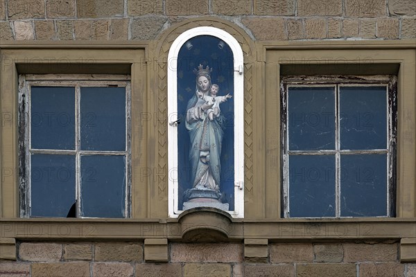 Figure of a saint on a house facade in a niche behind glass