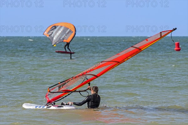 Female windsurfer entering the water and wingboarder