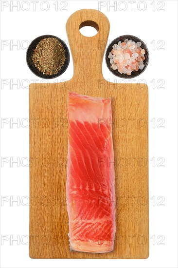 Piece of salmon fillet on wooden cutting board with salt and pepper