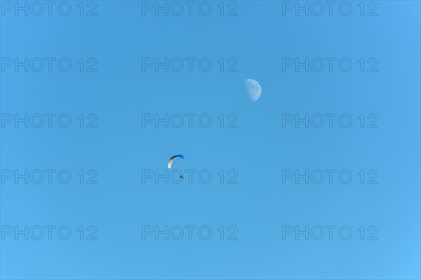 Paramotor in flight on a sunny day with the moon in the sky. France