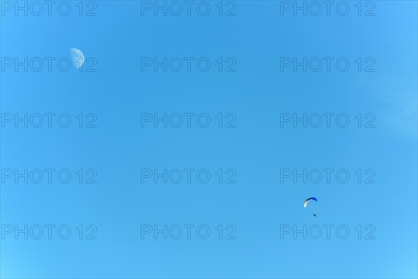 Paramotor in flight on a sunny day with the moon in the sky. France