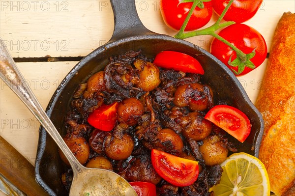 Baby cuttle fish roasted on iron skillet with tomatoes and onions over rustic wood table