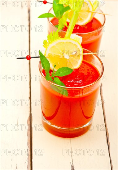 Fresh tomato juice gazpacho soup on a glass over white wood table