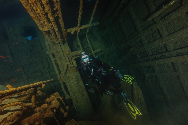 Female diver swims diving at railing of through hold of shipwreck wreck Elviscot at western tip of Elba