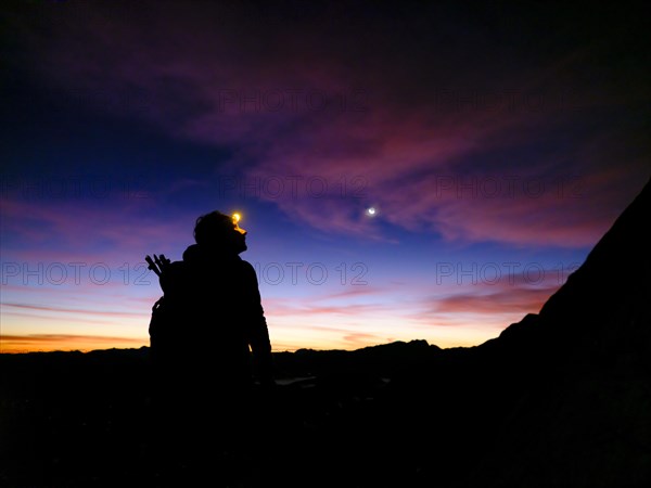 Silhouette of a female mountaineer with headlamp at dawn