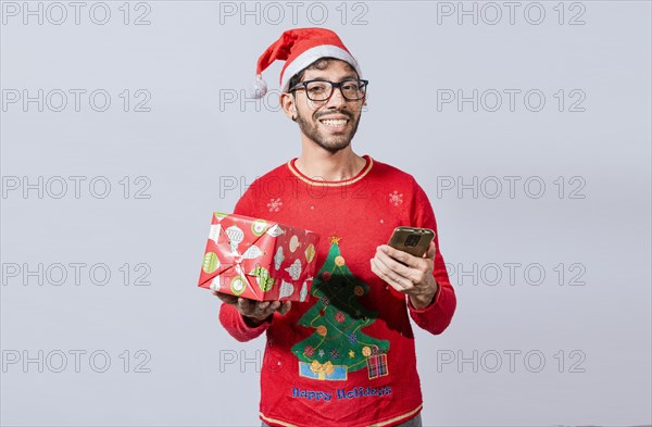 Handsome man in christmas hat holding gift and looking at phone