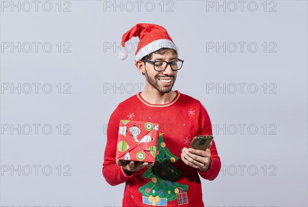 Christmas man holding gift box and telephone isolated. Handsome man in christmas hat holding gift and looking at phone