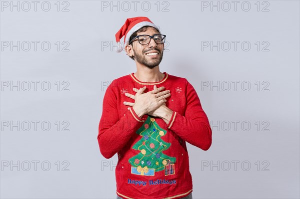 Thankful people in christmas clothes smiling with hands on chest. Man in christmas hat with sincere lovely smile feeling thankful