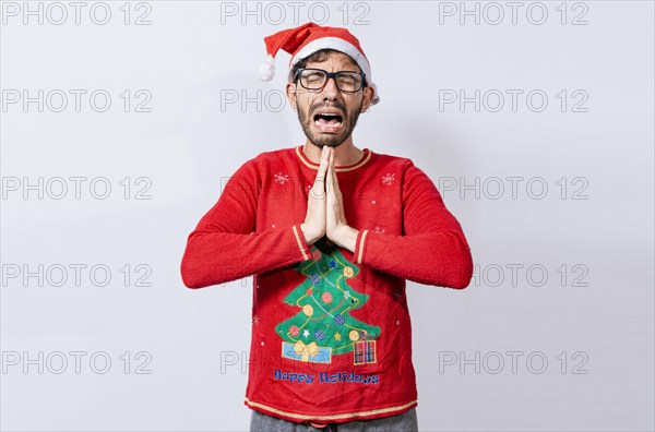 Man with christmas hat with hands together in pleading gesture. Christmas guy with hands together begging for a Christmas wish