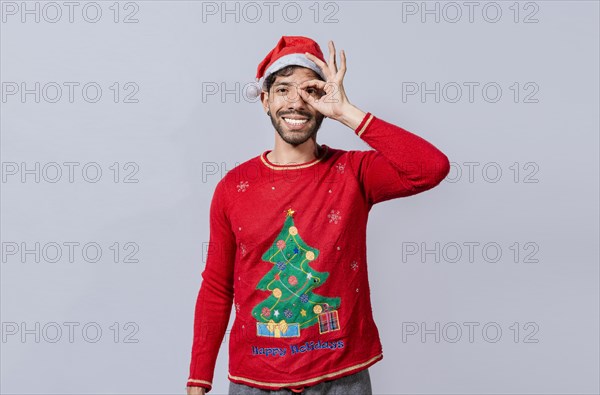 Funny young man in christmas hat looking through fingers. Funny christmas guy making gesture and looking through fingers