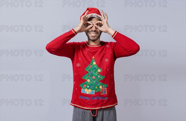 Man in christmas hat making gesture looking through fingers. Funny young man in christmas hat looking through fingers. Funny christmas guy making gesture and looking through fingers