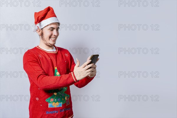 Happy guy in christmas hat smiling at cellphone isolated. People in santa hat using and smiling at cellphone isolated