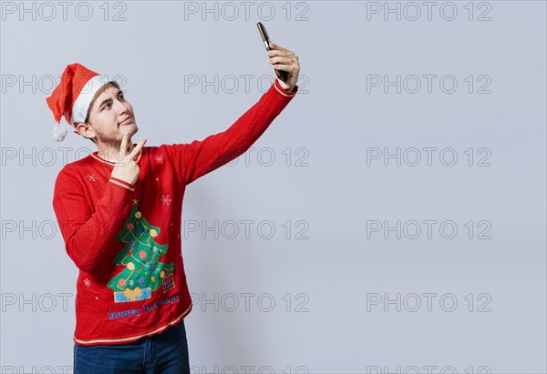 Happy handsome man in christmas hat taking a selfie. Happy guy taking a christmas selfie on isolated background