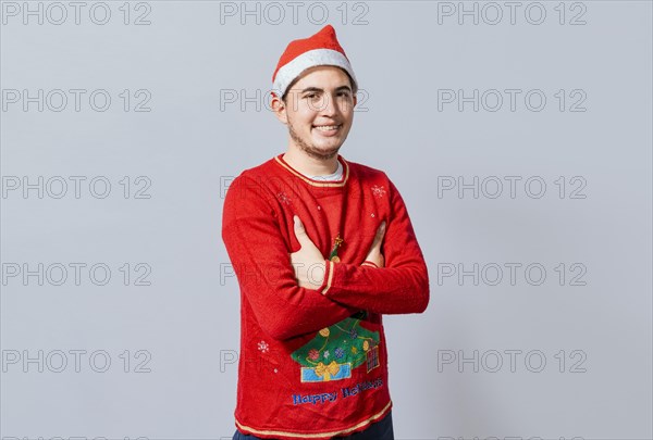 Portrait of guy in sweater and christmas hat with crossed arms isolated. Smiling guy in christmas hat with crossed arms smiling. Teenage guy in christmas clothes with crossed arms smiling