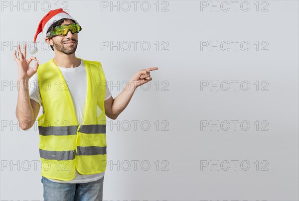 Engineer in christmas hat showing and recommending a product. Builder man in christmas hat pointing a christmas promo. Civil engineer in christmas hat recommending a christmas offer
