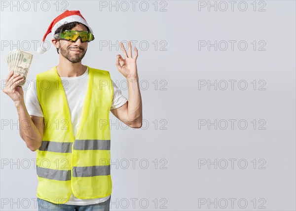 Engineer in christmas hat holding money in ok gesture. builder engineer in christmas hat with approving expression holding money bills. Christmas engineer concept holding money in happy holidays