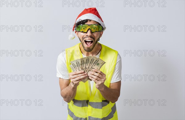 Engineer in christmas hat holding money smiling at camera. builder engineer in christmas hat with happy expression holding dollars isolated. Concept of engineer with money in holiday season