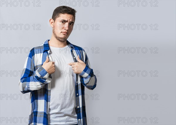 Confused caucasian young man pointing at himself. Confused person pointing at himself isolated. Confused latin guy pointing at himself isolated