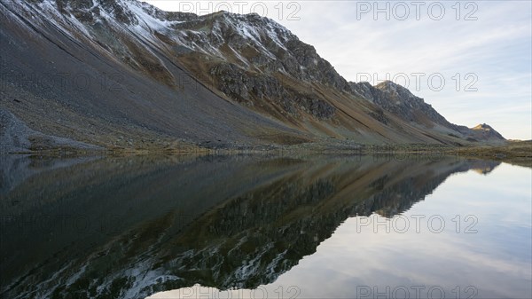 Slightly snow-covered mountains reflected in Lake Schotten in autumn at the Flueela Pass