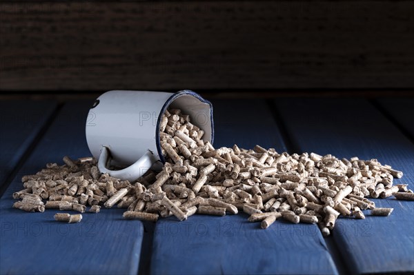 Wood pellets with enamel cup on blue wooden background