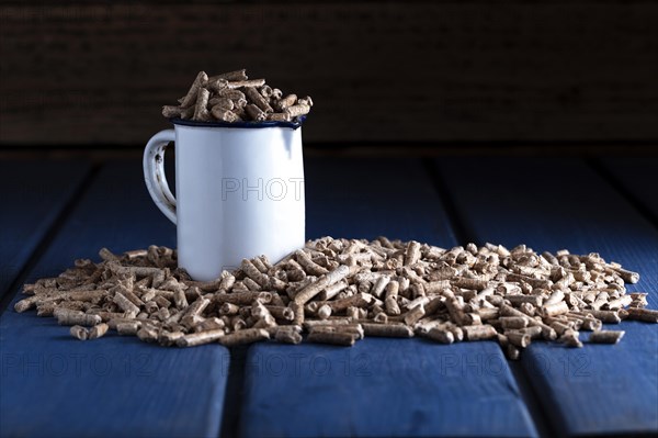 Wood pellets with enamel cup on blue wooden background