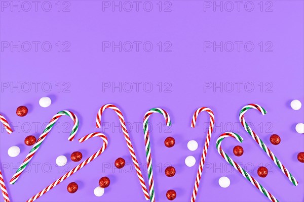 Christmas candy canes and ornament balls at bottom of purple background with copy space