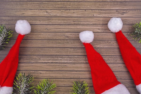 Seasonal Christmas flat lay with snow covered fir branches and red and white santa hats on wooden background with copy space