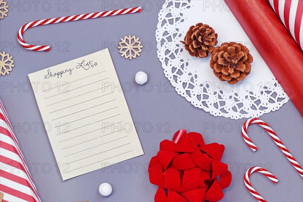 Flat lay design concept for buying Christmas presents with empty shopping list and seasonal decoration like candy canes