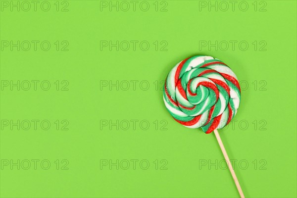 Lollipop with Christmas colors on green background with copy space