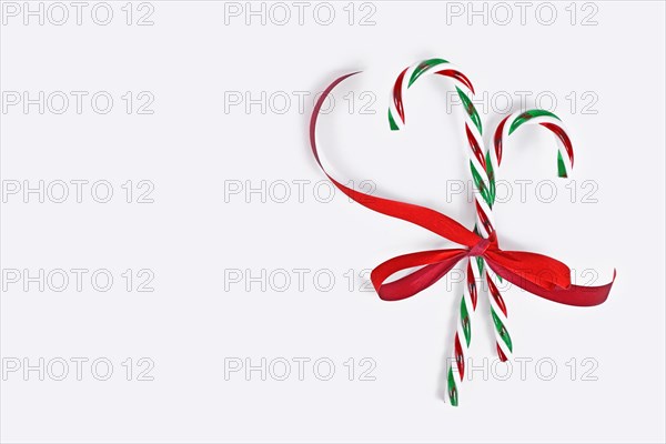 Striped candy canes tied together with red ribbon on side of white background with copy space