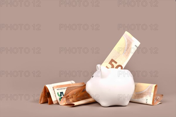 White piggy bank with 50 Euro bills on beige background with copy space. Concept for saving money