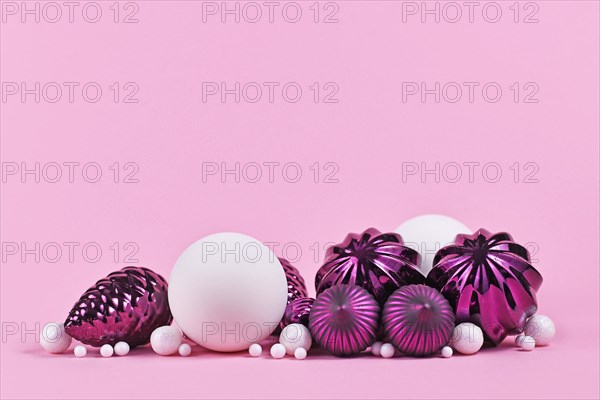 Christmas arrangement with purple and white tree ornament glass baubles on pink background with empty copy space